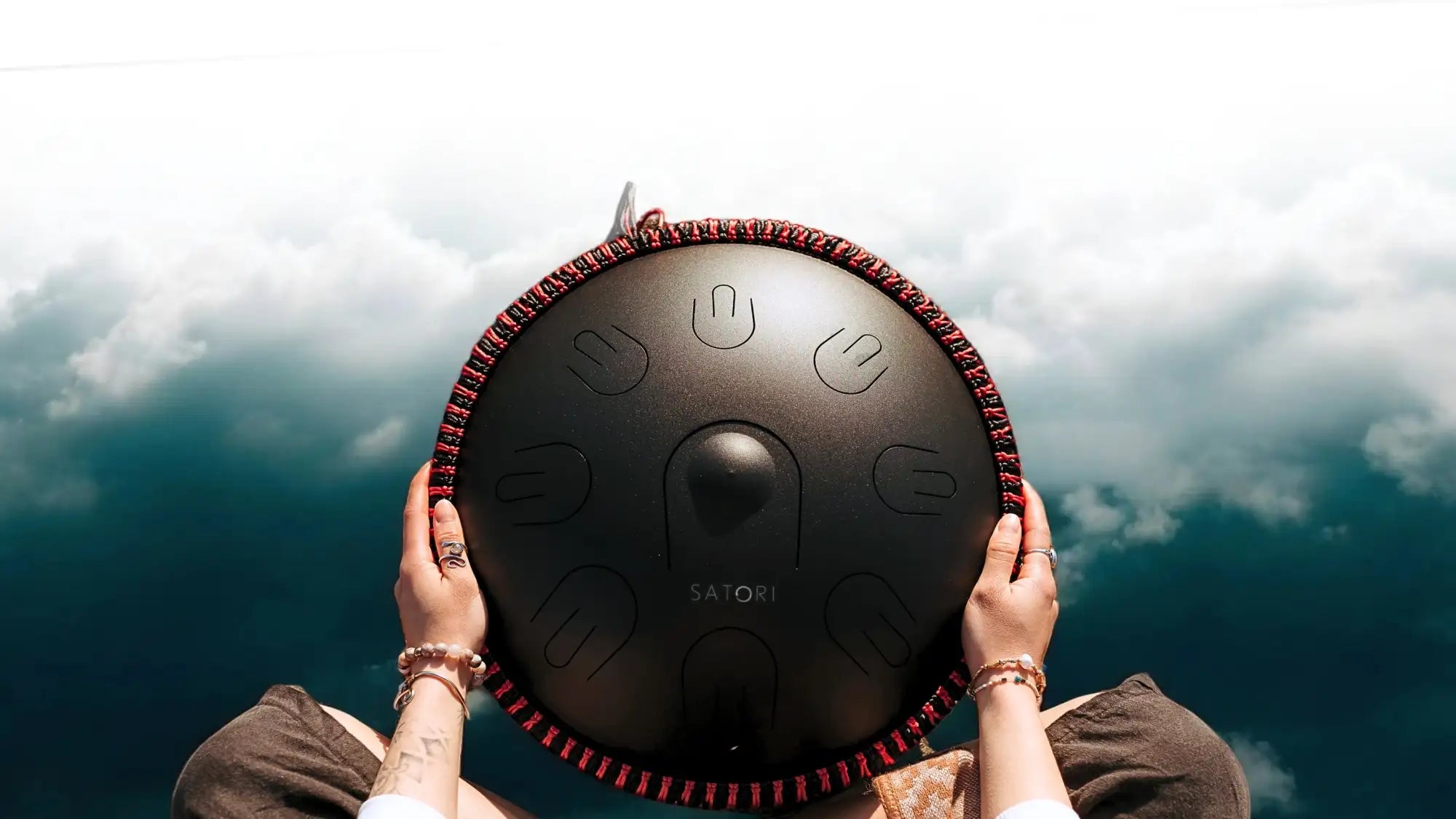Black satori handpan with red braided edge and engraved tuning marks.