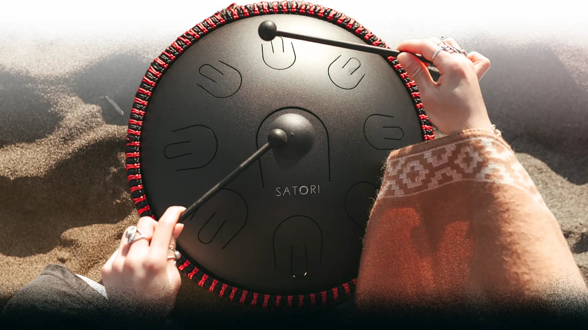 Black satori steel tongue drum with red braided edge and hand-stitched design, featuring embossed finger-shaped notes.