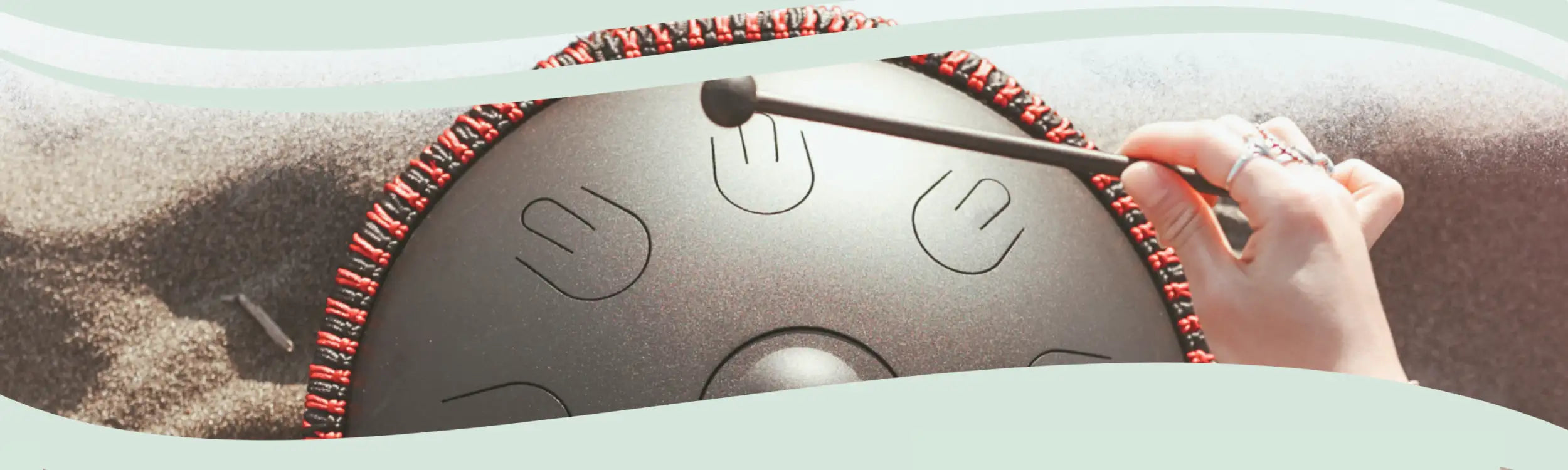 A sleek, dark gray handpan with red and black braided trim around its edge.